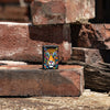 Lifestyle image of Zippo Tiger Stripes Design Black Matte Windproof Lighter standing on a brick with more bricks piled in the background.