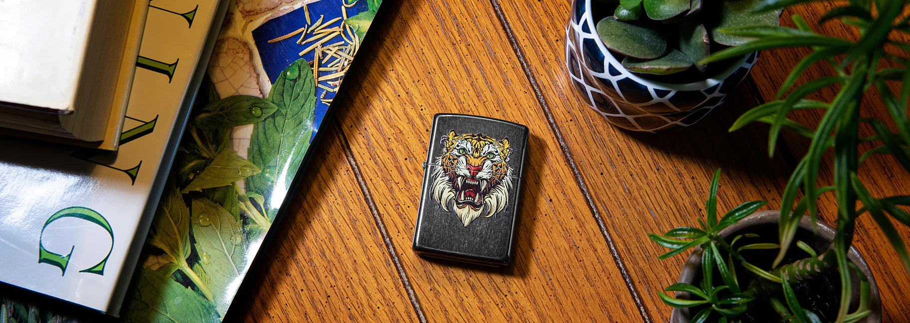 Plants and framed pictures of nature on a wood floor with a Zippo lighter in the middle with a lion design.
